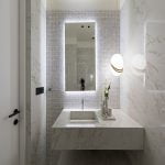 A bathroom with marble walls, a large mirror, and a porcelain shelf.