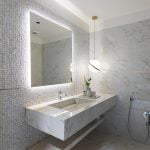 A bathroom with marble walls, a large mirror, and a porcelain shelf.