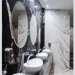 Three sinks with mirrors in a bathroom, featuring a sleek design with porcelain slab and a convenient shelf.