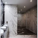 Three sinks with mirrors in a bathroom, featuring a sleek design with porcelain slab and a convenient shelf.